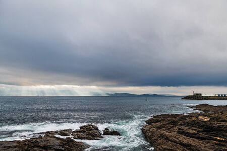Cliffs and small lighthouse on a cloudy Winter day in Portonovo in Galicia, Spain, with the entrance to the Ria de Pontevedra in the background.の写真素材
