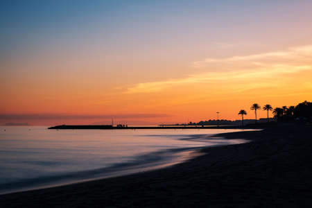 Sunset at a beach in the Costa del Sol in Marbella, Spain, with the silhouette of a pier and Gibraltar to be recognised in the background. Long exposure.の写真素材