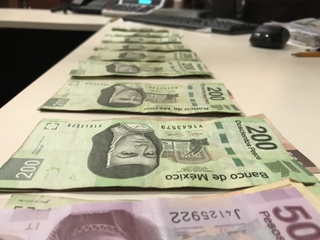 Many mexican pesos bills distributed and spread on a beige colored deskの写真素材