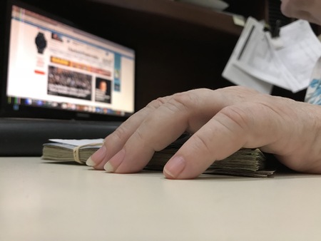 Many mixed Mexican peso bills on a beige desk and a hand touching them
