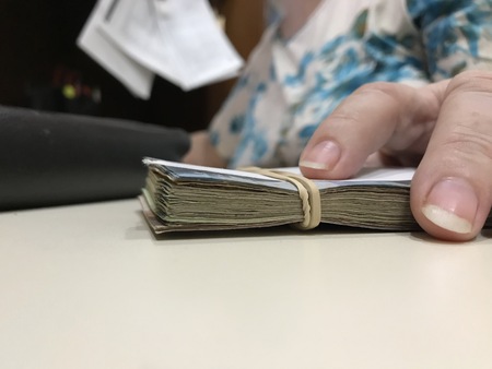 Many mixed Mexican peso bills on a beige desk and a hand touching them