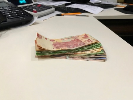Many mexican pesos bills spread over a beige colored desk inside a small business officeの写真素材
