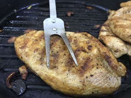 Piece of grilled chicken breast over a cast iron skillet with a meat fork on topの写真素材
