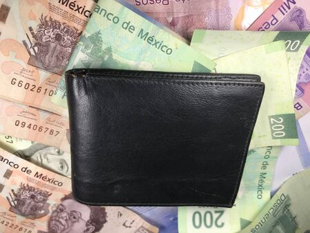 Many mexican pesos bills spread over a wooden desk inside a small business office