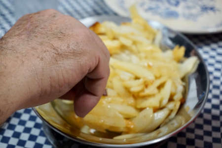 Male hand picking some fried potatoes on a blue and white surface