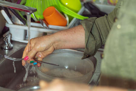 Person with colored nails washing a fork in the kitchenの写真素材