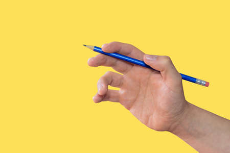 White hand holding a blue pencil on a yellow backgroundの写真素材