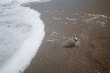 A glass bottle with sand inside half buried on the sea shore