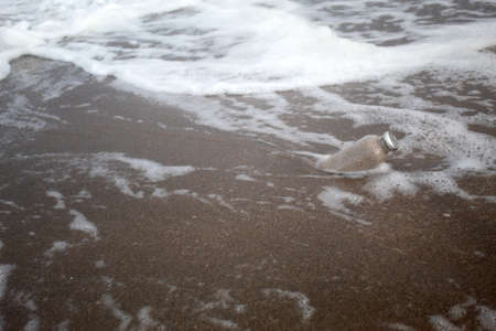 A glass bottle with sand inside half buried among small waves on the seashore