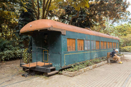 An isolated old train car with trees in the background and two unrecognizable people sitting on the...