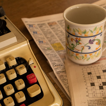 Close-up of a typewriter next to an empty coffee cup and newspaper sheets on the wooden tableの写真素材