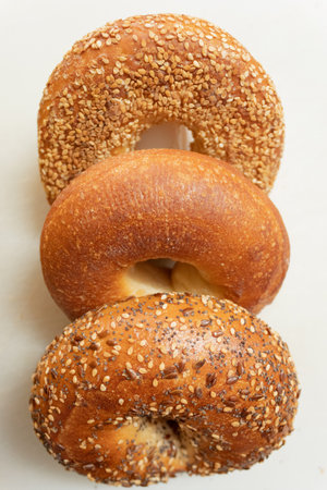 Three fresh bagels in a row on a white background. Sesame bagel, plane bagel and everything bagel.の写真素材