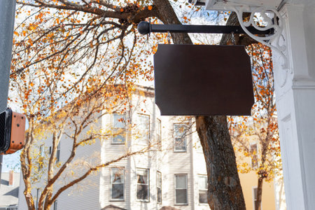 A blank wooden sign hanging outside a house with autumn trees in the backgroundの写真素材