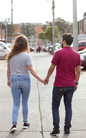 A heterosexual couple in love walking hand in hand on a street on a sunny day