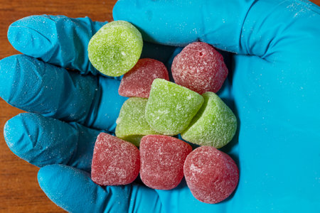 Close up of a shopkeeper's hand wearing a latex glove holding a small group of sugar gummies