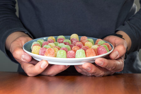 An unrecognizable man holding a plate full of colorful sugared gummiesの写真素材