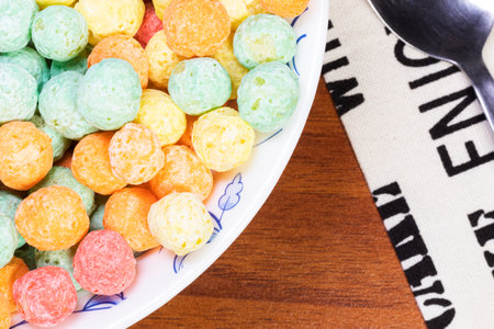 Close up overhead shot of a bowl of colorful sugary cereal next to a cloth napkin and spoon on a...
