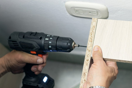 A man putting a screw with a driver screw drill into a cabinet