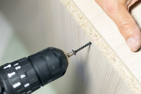 Close up of a man putting a screw with a drill driver to assemble a cabinetの写真素材