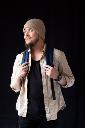 Bearded young college man smiling on a black background while holding his backpackの写真素材