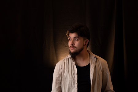 A young man with a beard in front of a dark background with empty space around
