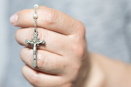 Close up of a white hand holding a silver rosaryの写真素材