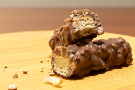 Close up of a chocolate and walnut covered nougat bar split in two on a wooden plate with some crumbsの写真素材