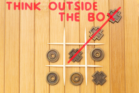 Copper tic tac toe game on a wooden background with red text: Think outside the box
