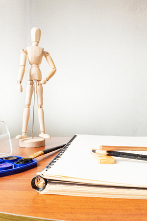 A draftsman's desk with a drawing mannequin, a sketchbook, pencils and watercolors. artist room.の写真素材