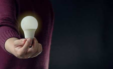 An unrecognizable business person holding an illuminated light bulb in the middle of the darkness with copy space. Enlightenment and idea generation concept.の写真素材