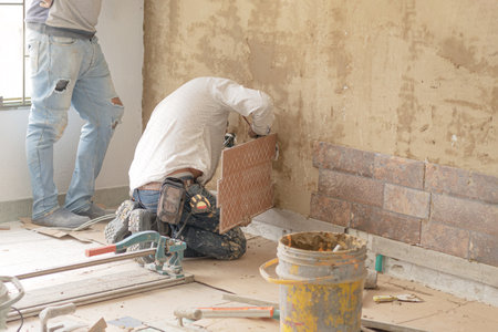 A foreman making measurements to install tiles on a wall, his assistant stands next to him. Home...