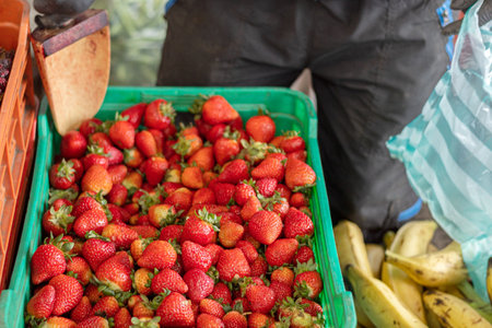 A person using a small shovel to pick some strawberries from a crate at a farmer's market. Organic food, ingredient for juices, smoothies and salads.の写真素材
