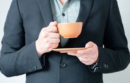 Close up of a businessman in a suit holding a cup of coffee and a small plate. Stress break at work,...