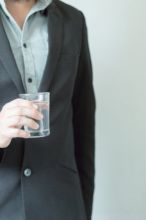 Man in suit without tie holding glass of water. Drink water, healthy practices. Pause at work.