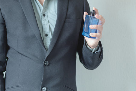 Man in suit using perfume on textured background. Personal care. Men's fragrances.