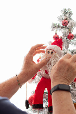 An unrecognizable woman decorates her Christmas tree on a white background. Santa Claus on the Christmas tree next to some red Christmas balls. End of year celebrations concept.の写真素材