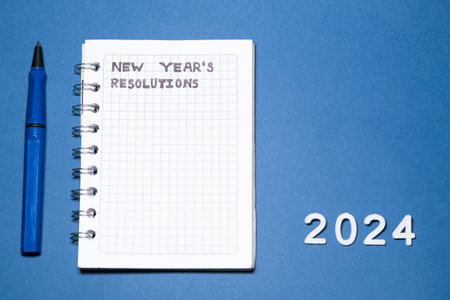 Blank New Year's resolution list in a small notebook on a flat blue background. Goals for the year 2024. Handwriting.の写真素材