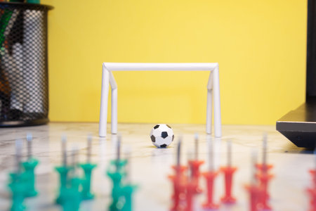 Tiny ball in front of a white goalpost on an office desk with a yellow background and thumbtacks in...