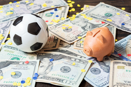 Soccer ball and piggy bank on dollar bills with confetti. Concept of soccer business, prizes, or sports bettingの写真素材