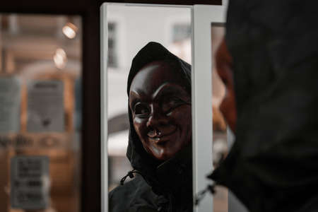 Reflection of a person in funny scary strange red mask with black jacket. Corona protective gear covid-19 style lifestyle rule of thirds creative art scary fear joke.の写真素材