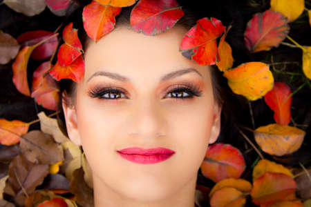 Beautiful young girl smiling while lying down in colorful autumn leavesの写真素材