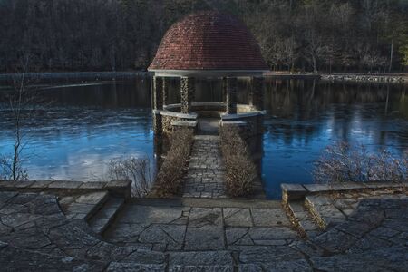 A spooky gazebo in the woods on a lake during the winter time.の写真素材