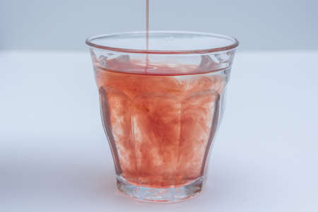 fruit juice extract poured into glass of water on white background