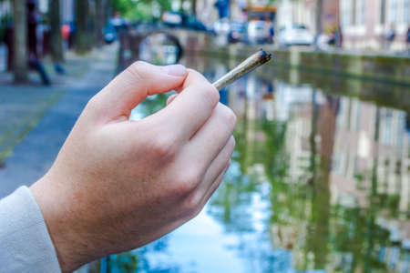 hand holding a cannabis joint on a canal in Amsterdamの写真素材