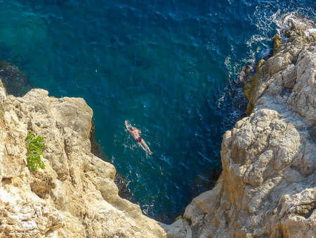 Dubrovnik, Croatia - August 4 2018: man swimming in open water near cliffs outside the old town walls of Dubrovnikのeditorial素材