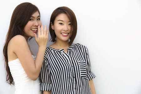 Two young Asian good friends sharing secrets の写真素材