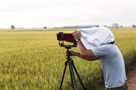 A photography hobbist with an old pavilion camera on a paddy field shooting sunrise 