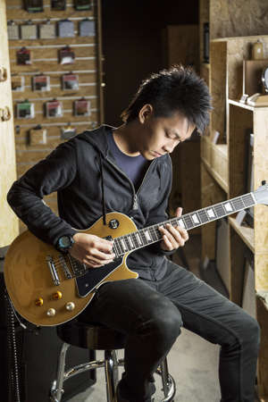 A vertical shot of a young asian man playing electric guitar.の写真素材