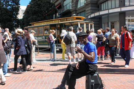 San Francisco, California, United States - 11 June 2010. Street musician and dancer sat on his electroacoustics relax and have a drink. People around are busy with their chores. Someone is waiting for the tram, some make photos, someone just walking.のeditorial素材