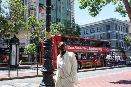 San Francisco, USA - 12 June 2010. Representative black man in a white suit walking down the street and smoking a cigar. Black man listening to music with headphones on the go.のeditorial素材
